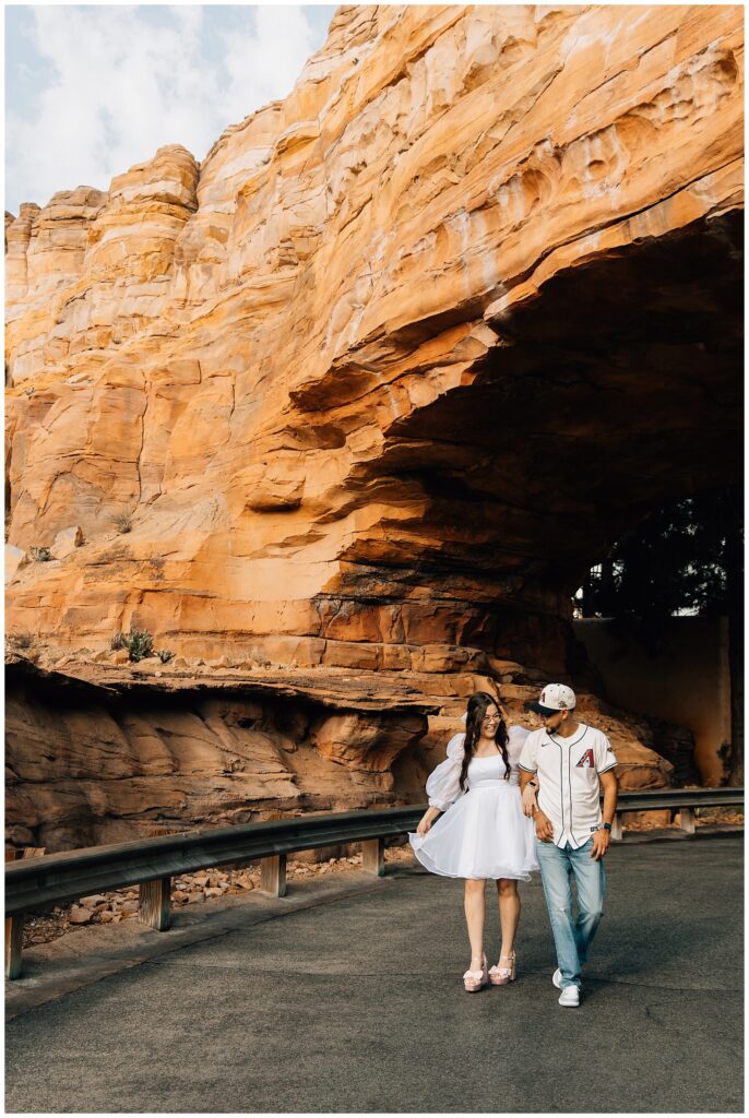 A couple walking through the desert-themed backdrop of Radiator Springs in Disneyland's California Adventure, sharing a moment as the woman in a white dress laughs alongside her partner, who is casually dressed in a baseball cap and jeans.