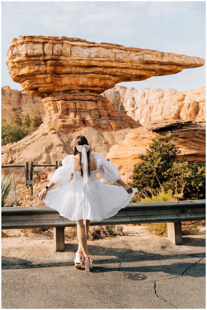 A solo shot of the woman in a white puffy-sleeved dress twirling in front of the Radiator Springs rock formation at Disneyland’s California Adventure, enjoying a whimsical and carefree moment.