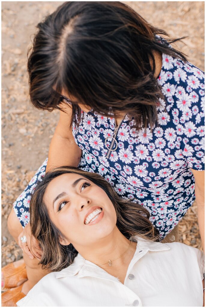 Daughter lying in her mother's lap, looking up at her with a joyful smile as they share a tender moment outdoors.