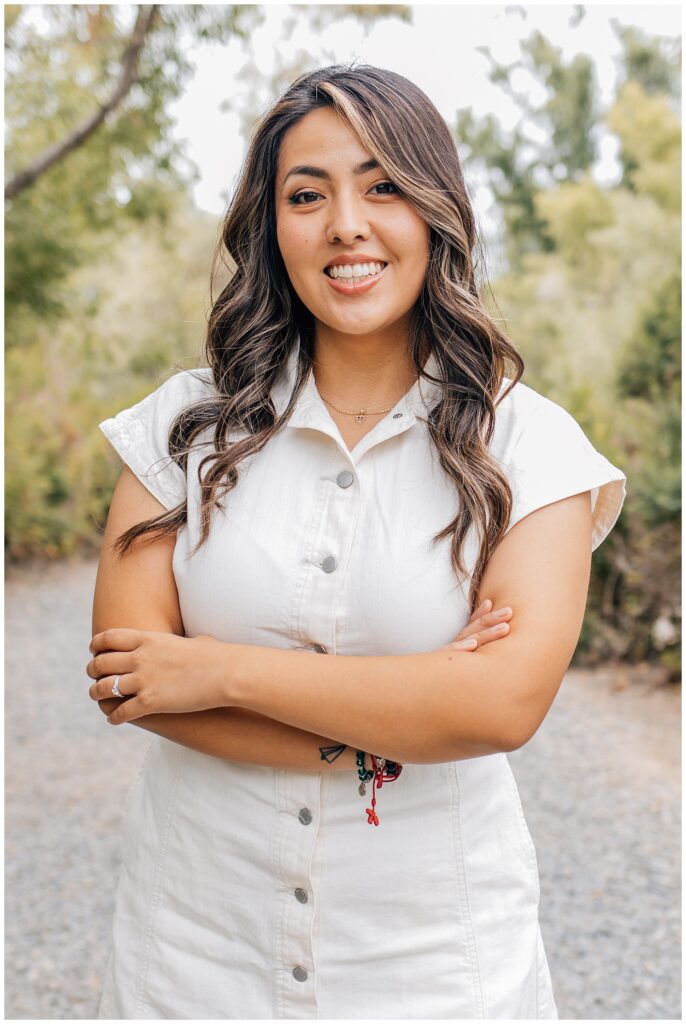 Portrait of the daughter standing with arms crossed, smiling confidently during an outdoor session on a gravel path.